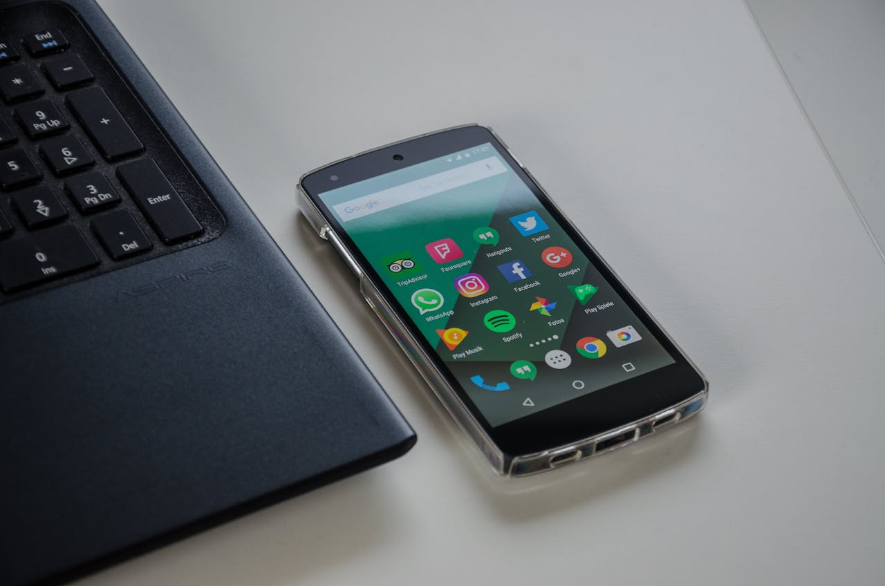 Smartphone on a table showing various social media apps beside a laptop keyboard.